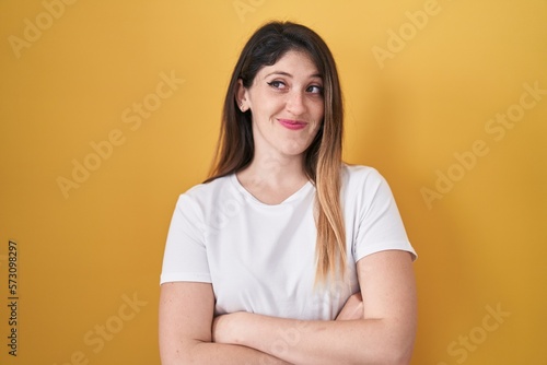 Young brunette woman standing over yellow background smiling looking to the side and staring away thinking.