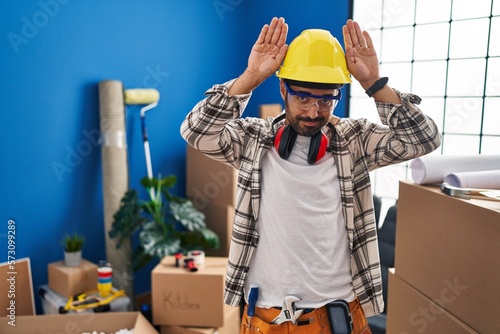 Young hispanic man with beard working at home renovation doing bunny ears gesture with hands palms looking cynical and skeptical. easter rabbit concept. photo