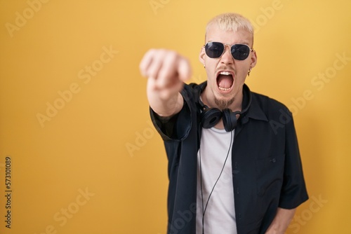 Young caucasian man wearing sunglasses standing over yellow background pointing displeased and frustrated to the camera, angry and furious with you