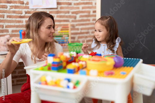 Teacher and toddler playing with construction blocks sitting on table at kindergarten