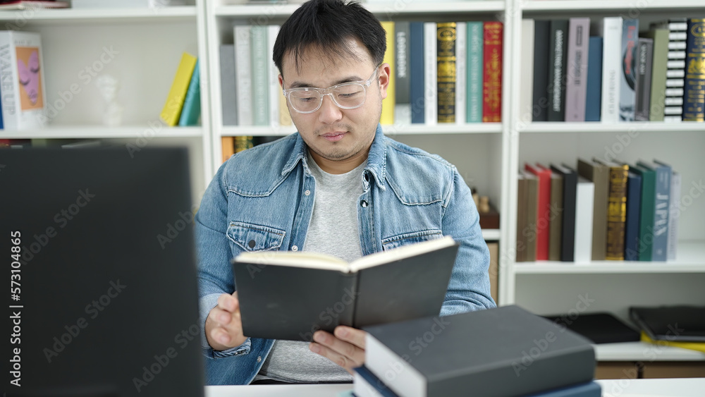 Young chinese man student reading book sitting on table at library university Young chinese man student reading book sitting on table at library university