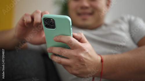 Young chinese man using smartphone sitting on sofa at home