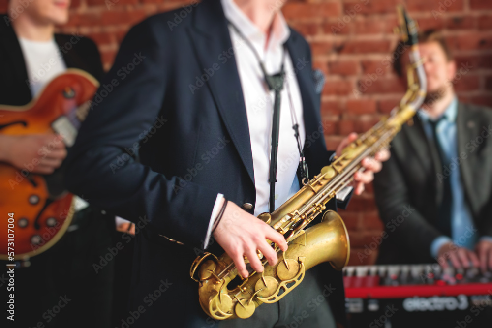 Fototapeta premium Concert view of saxophonist, a saxophone sax player with vocalist and musical band during jazz orchestra show performing music on a stage in the scene lights