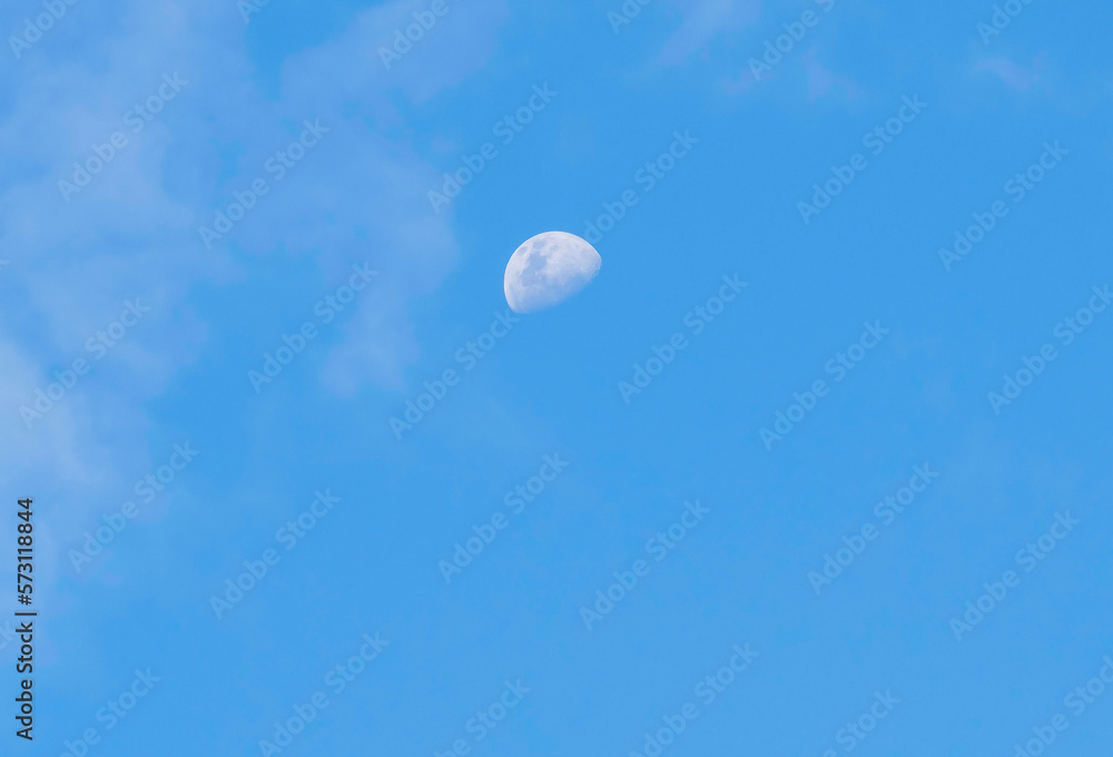 Late afternoon partial moon rising amongst the soft high cloud in the blue sky Late afternoon partial moon rising amongst the soft high cloud in the blue sky