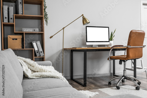 Interior of light office with table, modern computer and shelving unit