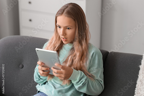 Shocked little girl using tablet computer on sofa at home
