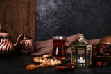 Muslim lantern with dates, glass of tea and prayer beads for Ramadan on dark background