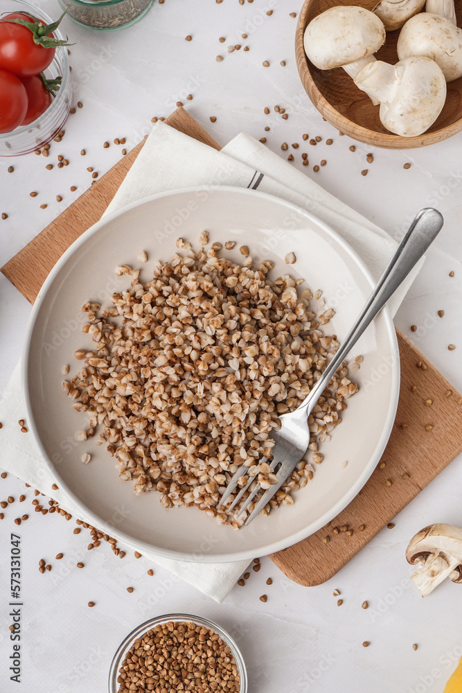 Board with plate of tasty buckwheat porridge on white table Board with plate of tasty buckwheat porridge on white table