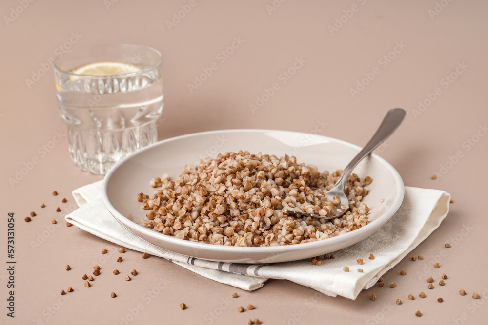 Napkin with plate of tasty buckwheat porridge and glass of water with lemon on beige background Napkin with plate of tasty buckwheat porridge and glass of water with lemon on beige background