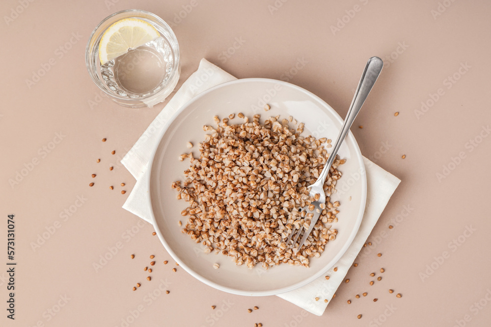 Napkin with plate of tasty buckwheat porridge and glass of water with lemon on beige background Napkin with plate of tasty buckwheat porridge and glass of water with lemon on beige background