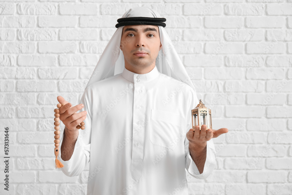 Muslim man with prayer beads and lantern near white brick wall Muslim man with prayer beads and lantern near white brick wall