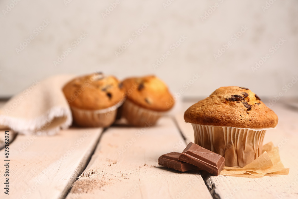 Tasty muffin and pieces of chocolate on light wooden table Tasty muffin and pieces of chocolate on light wooden table