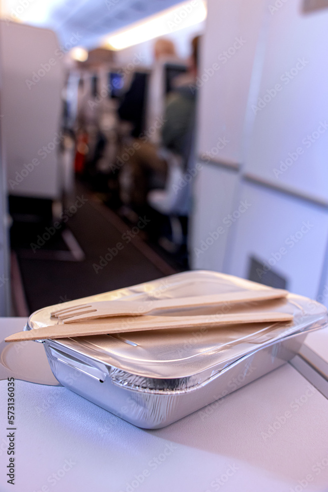 Hot meal in a foil box with wooden cutlery on a passenger's table in a flying plane Hot meal in a foil box with wooden cutlery on a passenger's table in a flying plane