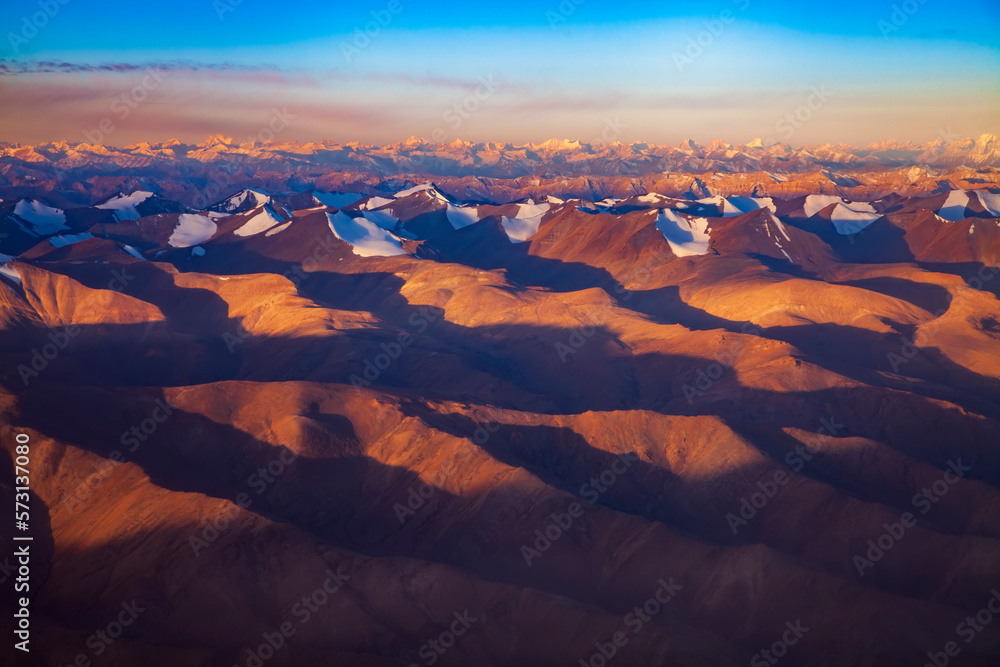 Winter aerial landscape of snow cap mountain in sunrise. Karakorum or Himalaya mountain from above in morning.Sunlight touch the peak of summit with clear blue sky.Mountain in Leh Ladakh,India.