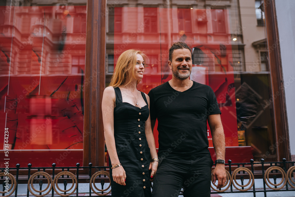Young adult European couple in black clothes standing in city walking, traveling on honeymoon. Pretty redhead Irish woman dating Hispanic man. Romance, relationship. Cheerful guy with wife outside.