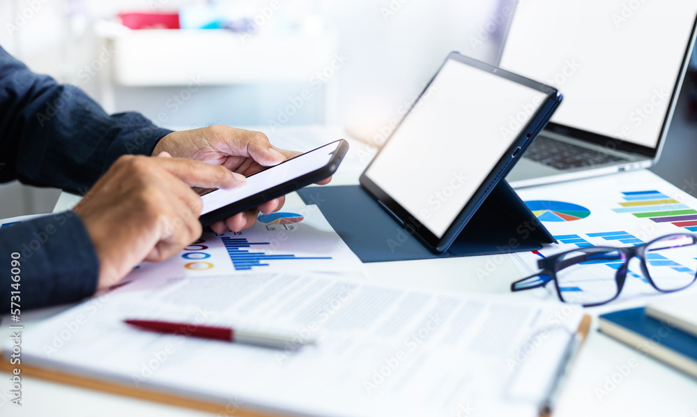 Asian businessman using smart phone to searching stock market data, Successful business people using laptop and tablet computer to analysis investment plan with chart on paperwork, Close-up view Asian businessman using smart phone to searching stock market data, Successful business people using laptop and tablet computer to analysis investment plan with chart on paperwork, Close-up view