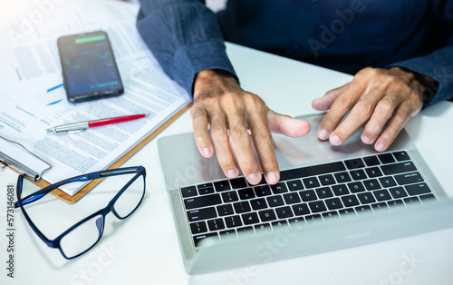 Close-up view, successful businessman, manager or freelancer working on desk at office using laptop, checking work papers and analysis digital chart on mobile