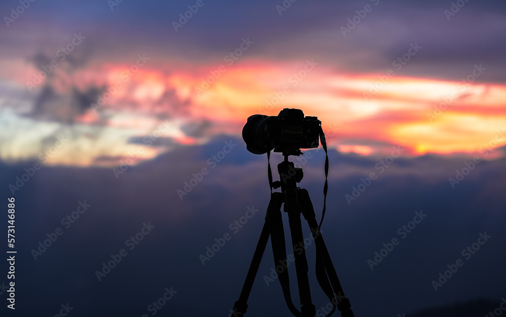 Photographing the sunrise. Silhouette of a professional camera on a tripod against amazing sunrise sky in background.