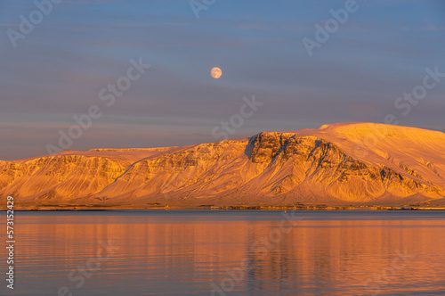 Sunset from the Reykjavik city waterfront promenade showing the full moon and the snow-capped and orange-lit islands of Engey and Videy reflected in the sea by the evening sun photo