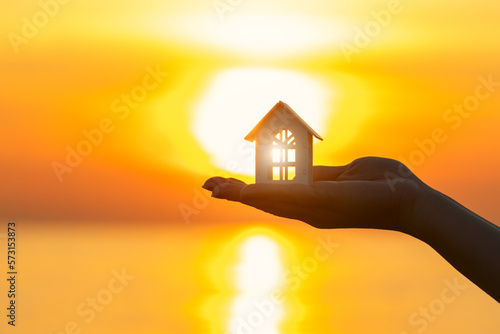 property insurance, real estate agency, mortgage, hand holding a house against the background of a sea sunset