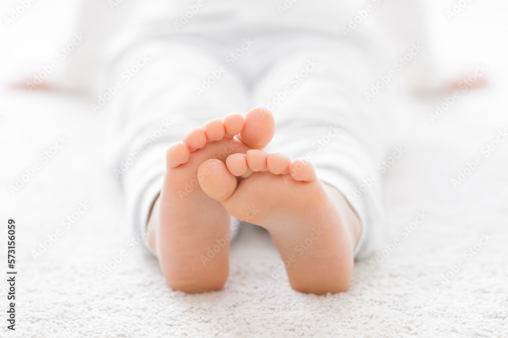 Little child in white clothes sitting and relaxing on light carpet at home room. Barefoot closeup. Front view. Little child in white clothes sitting and relaxing on light carpet at home room. Barefoot closeup. Front view.