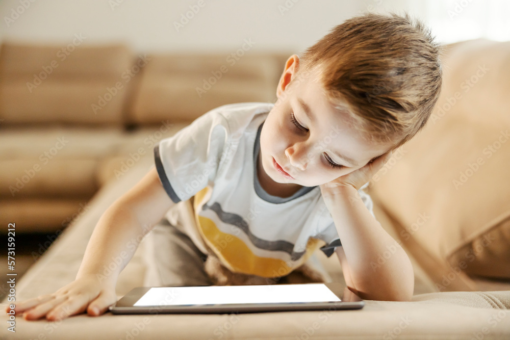 Youngsters and technology addiction. A young boy is wasting his time by watching videos on tablet at home. Youngsters and technology addiction. A young boy is wasting his time by watching videos on tablet at home.