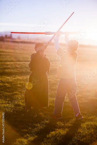 Two, 6 year old boys play light sabers (Star Wars) battles in a field at sunset. One boy is in a Jedi robe. photo