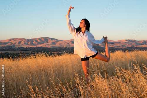 Woman balancing in a field of golden grass in sun drenched hills of California. photo