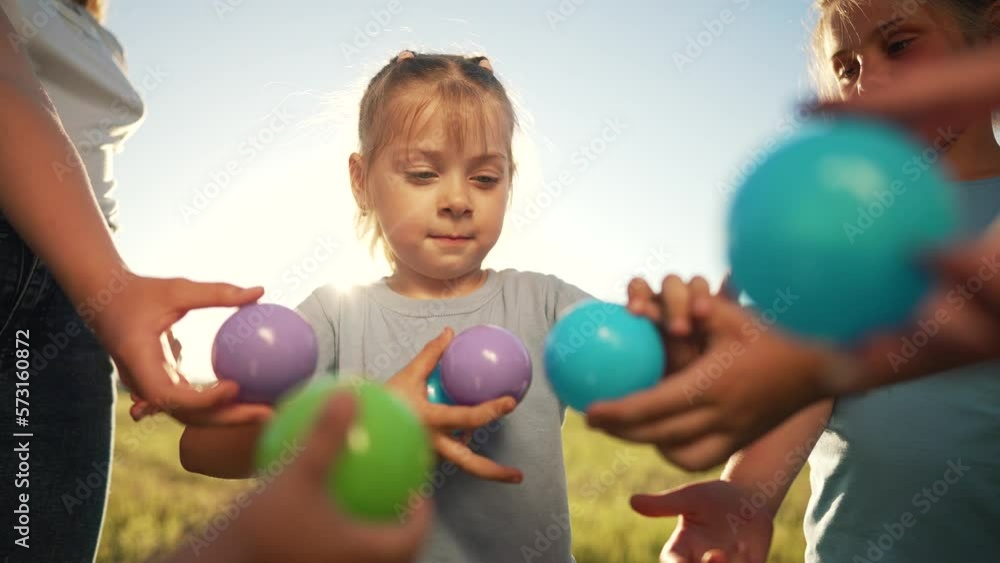 Happy children play together and have fun in the park with colorful balls. Girl collects small balls from children. Teamwork of children in park on the grass. Happy child playing with colored balloons Happy children play together and have fun in the park with colorful balls. Girl collects small balls from children. Teamwork of children in park on the grass. Happy child playing with colored balloons