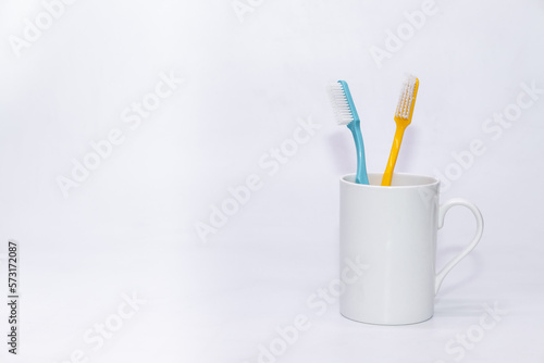 A pair of colorful toothbrushes kept inside a white cup with white copy space background 