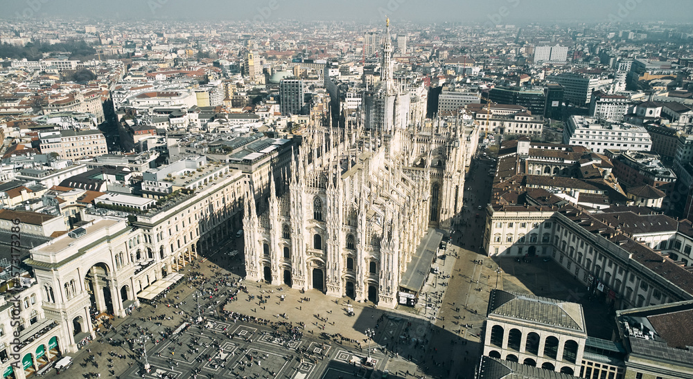 Fototapeta premium Aerial view of Piazza Duomo in front of the gothic cathedral in the center. Drone view of the gallery and rooftops during the day. Milan, Italy. High quality photo