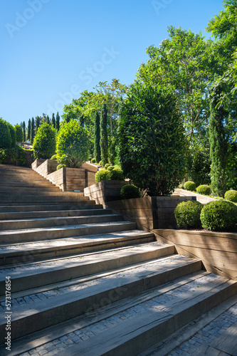 Stairs in the city park with bushes and trees on a sunny summer day with shadow. © Kufotos