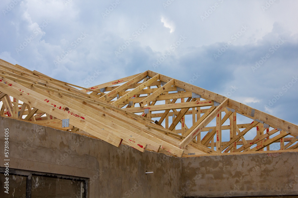Unpainted plaster walls and wooden roof beams of a house under construction with thunderstorm clouds in the background. 