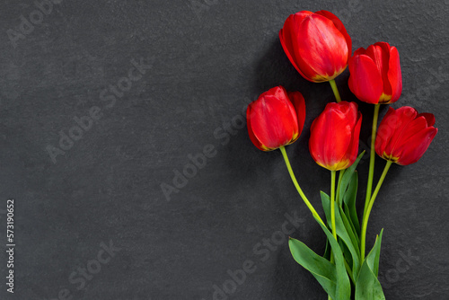 Bouquet of beautiful red tulips on black granite monument with empty space for text.