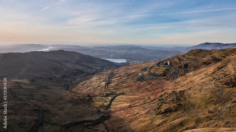 Beautiful aerial drone landscape image of sunrise Winter view from Red Screes in Lake District looking towards Windermere in the distance over Wansfell Pike peak