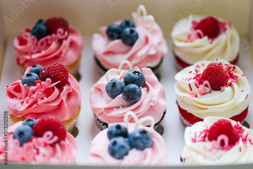 Fresh and delicious cupcakes with cheese cream and fresh berries. Top view of arranged tasty cupcakes in cardboard box isolated on white. Cakes with cream, chocolate bars, blueberries and raspberries 