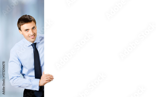 Portrait image of business man professional bank manager in confident cloth, necktie stand behind show empty white banner signboard billboard with copy space text area. Blurred office background.