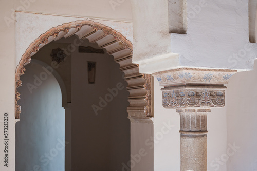 Ornate column with blue painted details with traditional arched doorway in the background at Nasrid Palace, Alcazaba, Spain