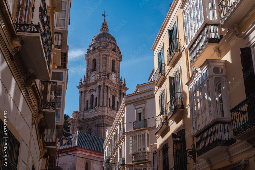 Malaga Cathedral's north tower built in Gothic, Renaissance, and Baroque style captured from a narrow street bustling with locals and tourists
