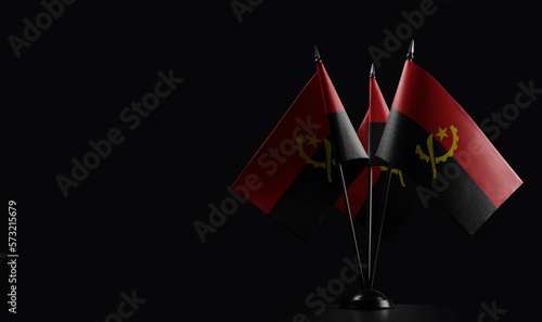 Small national flags of the Angola on a black background