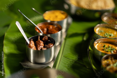 An assortment of traditional Indian seasonings — curry chilis; pickles; and 'gunpowder' splice blend ('milagai podi') — against a backdrop of banana leaves, suggesting southern Indian cuisine.