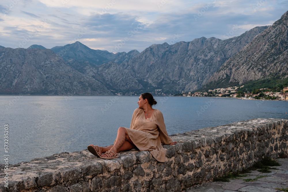 beautiful woman in a dress, sitting on a side, admiring the landscape, Kotor bay, Montenegro 