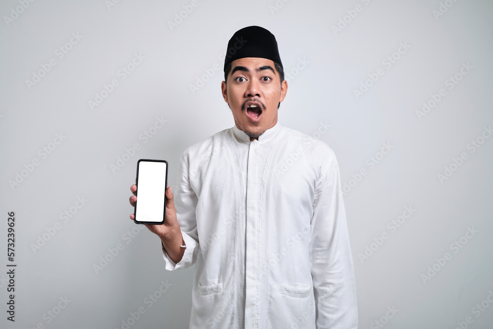 Surprised young Asian Muslim man showing empty display mobile phone screen isolated on white background Surprised young Asian Muslim man showing empty display mobile phone screen isolated on white background
