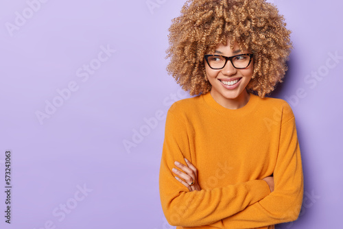 Canvas-taulu Waist up shot of positive curly haired woman keeps arms folded stands in self as
