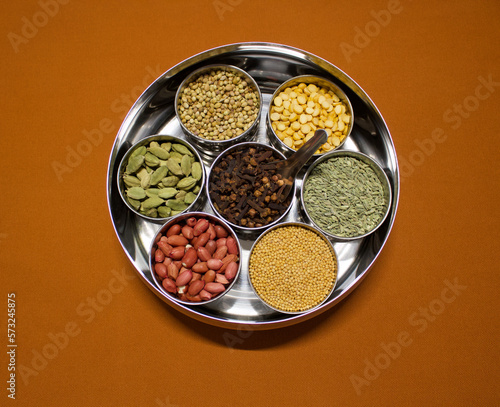 Indian spices and herbs in a container box masala dabba on an orange background, top view