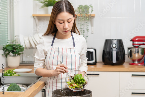 Compost from leftover food asian young housekeeper woman  female hand holding salad bowl use fork scraping waste  rotten vegetable throwing away into garbage  trash or bin. Environmentally responsible