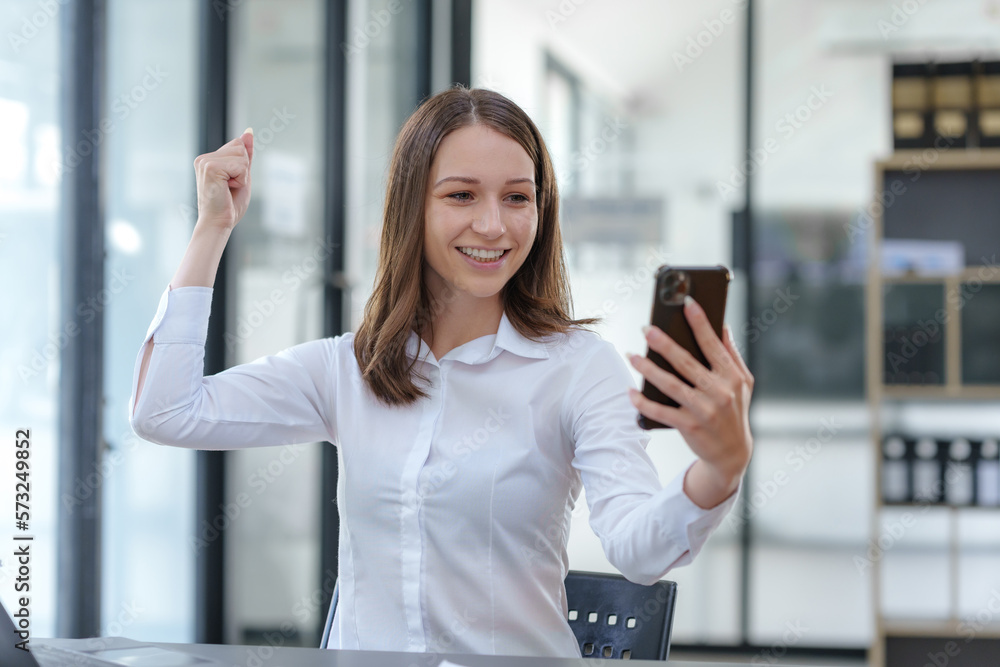 Beautiful business woman using smartphone is delighted and excited by the success she has achieved through her office cell phone.