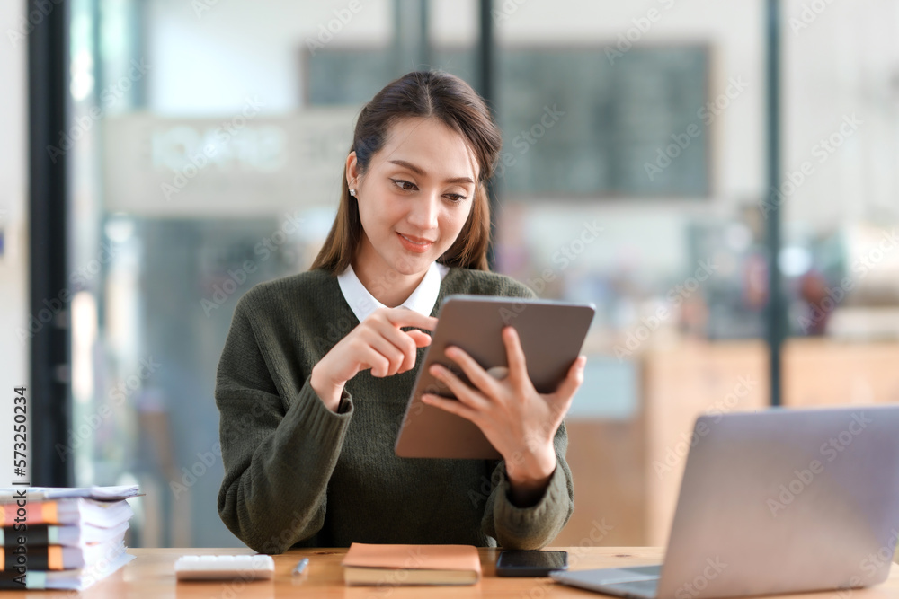 Attractive Asian businesswoman sitting happily using tablet at work and smiling happily. Attractive Asian businesswoman sitting happily using tablet at work and smiling happily.