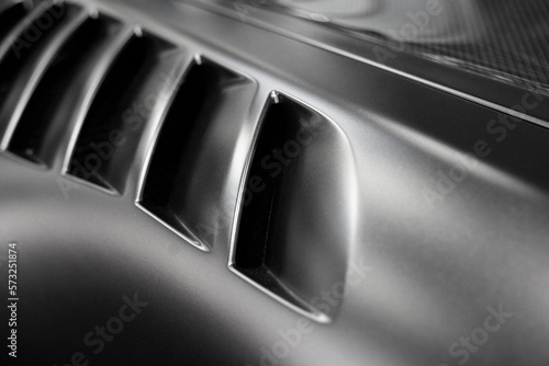 detail of black sport car with dark metal hood and air flow intake ornament