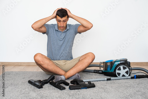 Tablou pe pânză A man at home chooses exactly which brush to attach to the vacuum cleaner